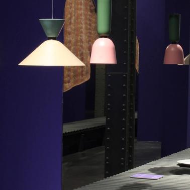 A modern display of various hanging lamps with different shades above a dark table in a room with purple walls.