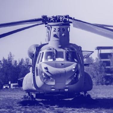 A blue-tinted photo of a military helicopter parked on a grassy field.