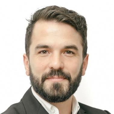 Portrait of a smiling man with a beard and professional attire against a white background.