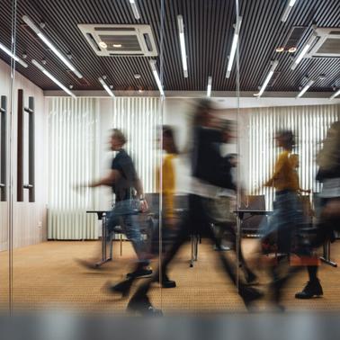 Blurry motion of busy people walking in a modern office corridor with wooden decor and glass partitions.
