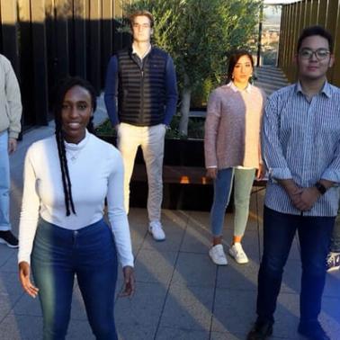 A group of six diverse young adults standing outdoors, with one woman in the foreground.