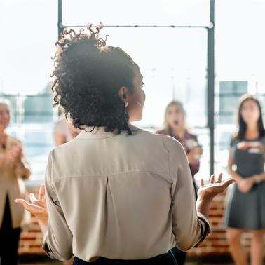 A woman is giving a presentation to a group of attentive colleagues in a brightly lit office space.