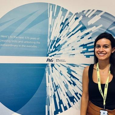 A woman smiling in front of a corporate anniversary banner that reads 'Here's to the next 175 years of creating firsts and unlocking the extraordinary in the everyday.'