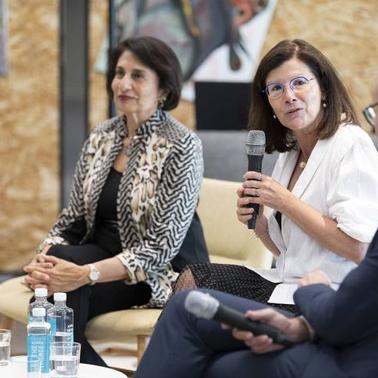 A woman speaks into a microphone during a panel discussion while seated next to other panelists.