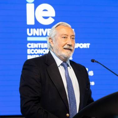 An older man with a beard is giving a speech at a podium with a blue background featuring European Union and IE University logos.