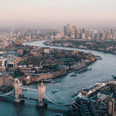 Aerial view of London showing the River Thames, Tower Bridge, and skyscrapers in the financial district during sunset.