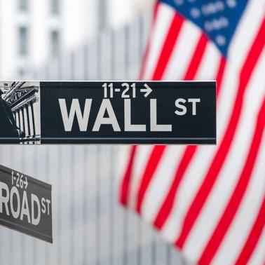Street signs for Wall Street and Broad Street with American flags in the background.