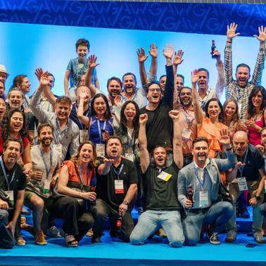A vibrant group of people celebrating together with raised hands and smiles at an event.