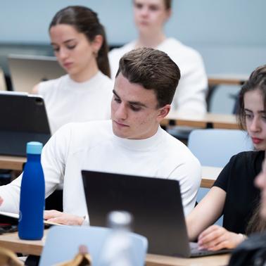 A group of students engaged in a classroom setting using laptops and taking notes.