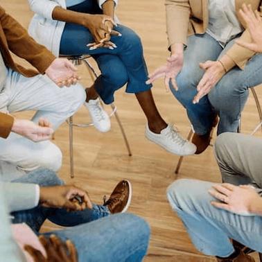A group of people sitting in a circle, gesturing with their hands during a discussion or activity.