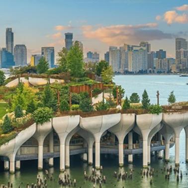 A scenic view of a modern waterfront park with lush greenery and a city skyline in the background.