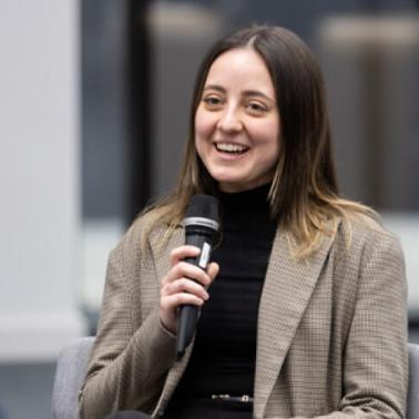 A woman smiles while holding a microphone in a discussion panel setting.