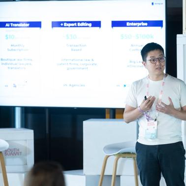 A person presenting at a tech conference with a slide showing service pricing behind them.