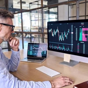 A man analyzing financial data on multiple computer screens in a modern office setting.
