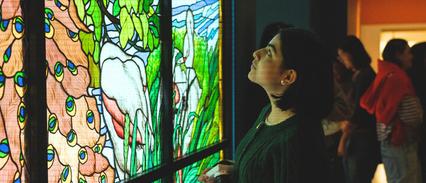 A woman admires a colorful stained glass window in a museum.