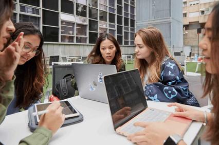 A group of young women studying together outdoors with laptops and tablets.