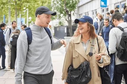 A young man and woman in casual clothes talking and laughing while walking on a busy street.