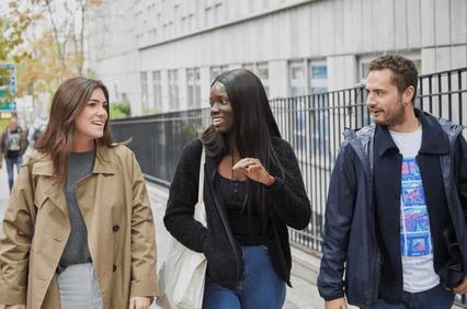 Three friends walking and talking happily on a city street.