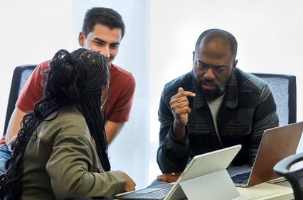 A group of three people engaged in a discussion around laptops in a modern office environment.