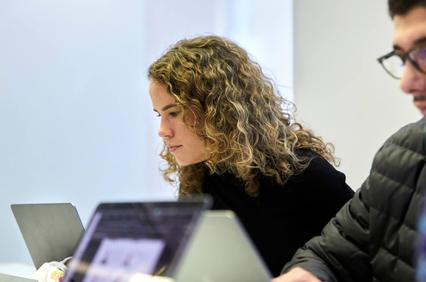 A woman with curly hair is focused while working on a laptop in a modern environment.