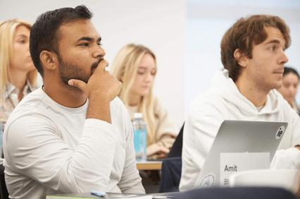 A group of students attentively listening in a classroom setting, with one particularly focused individual in the foreground.