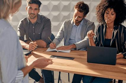 A group of four professionals sitting around a table, engaged in a serious discussion with notes and a laptop.