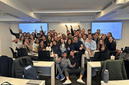 A large group of people is happily posing for a photo in a classroom setting.