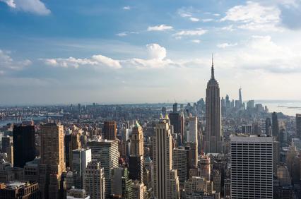 A panoramic view of a city skyline featuring tall buildings and a prominent skyscraper under a blue sky.