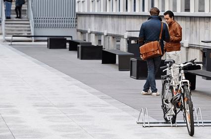Two men talking beside a parked bicycle on an urban walkway.