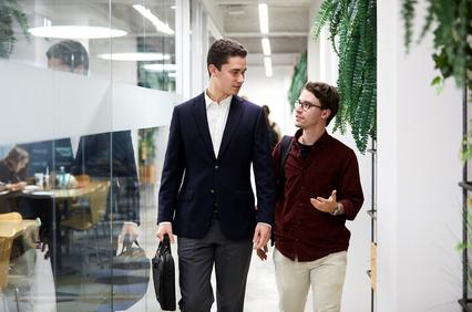 Two men walking and talking in a modern office corridor.