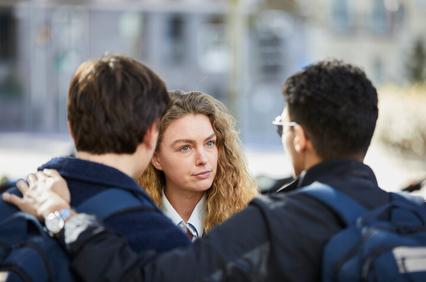 A young woman is listening intently to two boys who are facing her, in a casual outdoor setting.