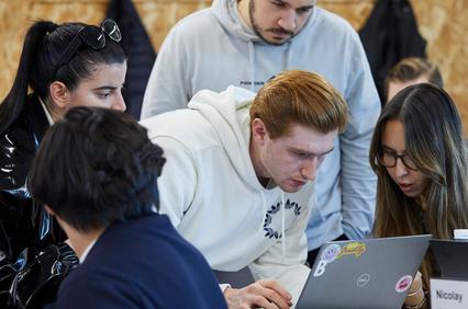 A group of young people collaborating on a laptop in a casual workspace.