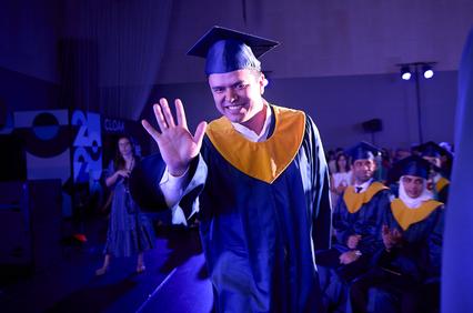 A graduate in a cap and gown waves to the audience during a ceremony.