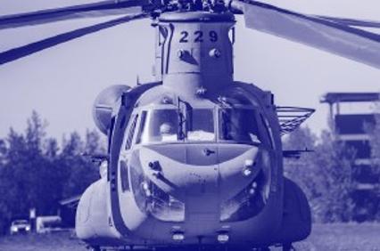 A blue-tinted photo of a military helicopter parked on a grassy field.