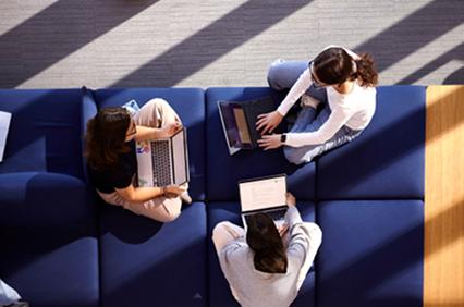A group of three individuals working collaboratively on laptops in a bright setting.