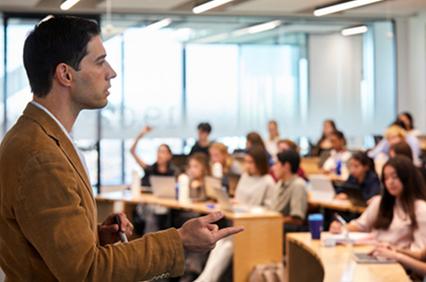 A speaker presents to a seated audience in a classroom setting.