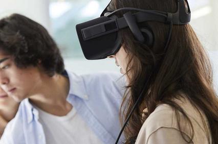 A young woman wearing a virtual reality headset with a young man looking on in an indoor setting.