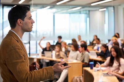 A speaker presents in front of an engaged audience in a classroom setting.