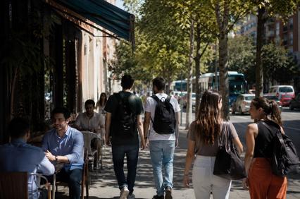 A busy street scene with people walking, enjoying outdoor seating, and public transportation in the background.