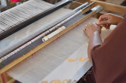 A person is weaving fabric on a traditional handloom, focusing on the intricate details of the pattern.