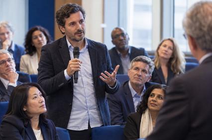 A man is speaking into a microphone during a conference while the audience listens intently.