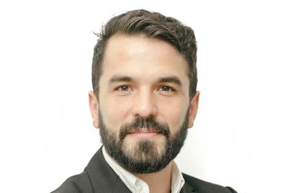 Portrait of a smiling man with a beard and professional attire against a white background.