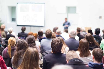 A large audience attentively listening to a speaker during a presentation.