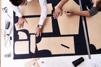 Two people working on tailoring patterns on a large piece of fabric, with measuring tools and scissors around them.