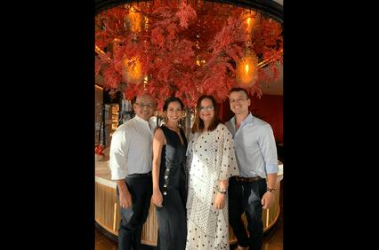 Four people posing for a photo in a restaurant with a vibrant red autumnal tree decoration in the background.