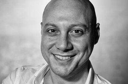 Black and white portrait of a smiling bald man wearing a white shirt.