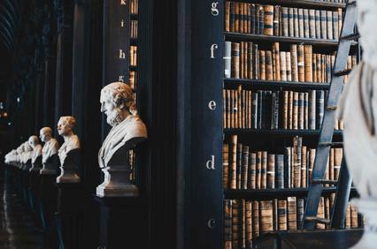 A row of classical bust sculptures positioned before shelves filled with aged books inside a historic library.