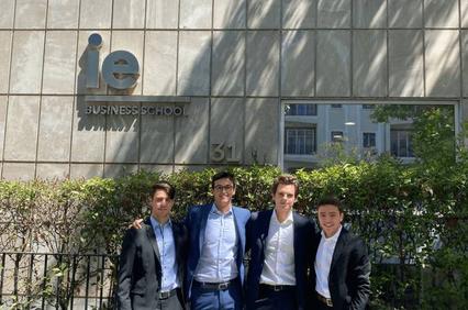 Four young men in business attire standing in front of the IE Business School building.