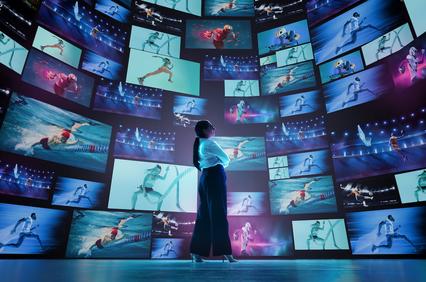 A person stands in front of multiple screens displaying various sports activities.
