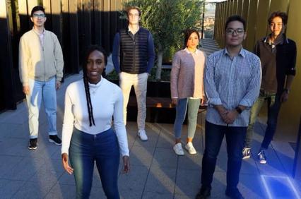 A group of six diverse young adults standing outdoors, with one woman in the foreground.